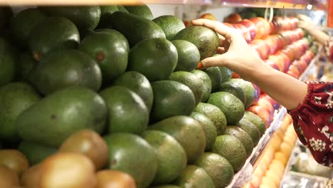 mujer seleccionando aguacates en una tienda de comestibles