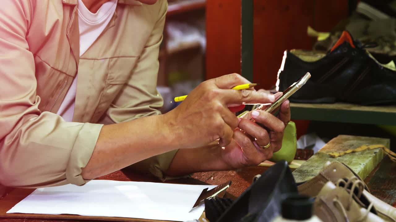 сапожник замечает на бумаге, используя мобильный телефон