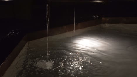 Close-view-of-the-jet-of-a-stone-fountain-falling-in-the-water-during-the-night