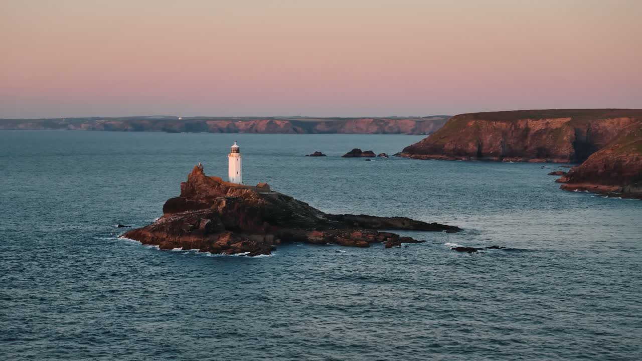 Drone flies wide circle right away from Godfrey’s Point Lighthouse into ocean horizon at sunset, pullback establishing