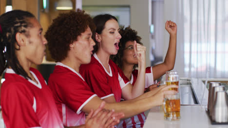 Diverse-group-of-happy-friends-watching-a-game-raising-glasses-making-a-toast-at-a-bar