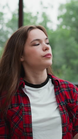 la mujer triste ajusta el peinado contra la ventana. la dama bonita en camisa a cuadros quita el cabello suelto de la cara en la terraza del edificio. estilo de belleza casual