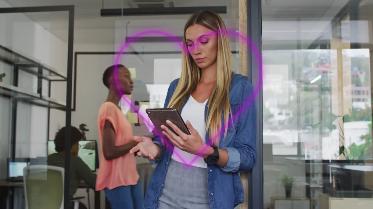 Purple heart outline highlighting focus on blonde woman, colleague walking gesturing in tech office