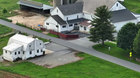 growing farm plantation fields in front of large farmstead with silo. drone shot on cloudy day in pennsylvanian countryside. stable, barn and greenhouse in rural area of usa. aerial rising shot.