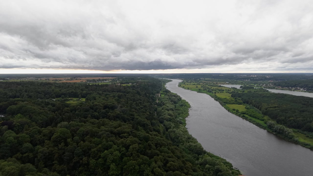 Vídeo de drone sobrevoa um rio largo serpenteando por florestas verdes exuberantes e paisagem rural sob céus dramaticamente nublados, exibindo paisagens naturais em detalhes vívidos e luz do dia suave