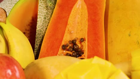a close-up view of assorted tropical fruits including papaya, mango, apple, and banana on a textured background.