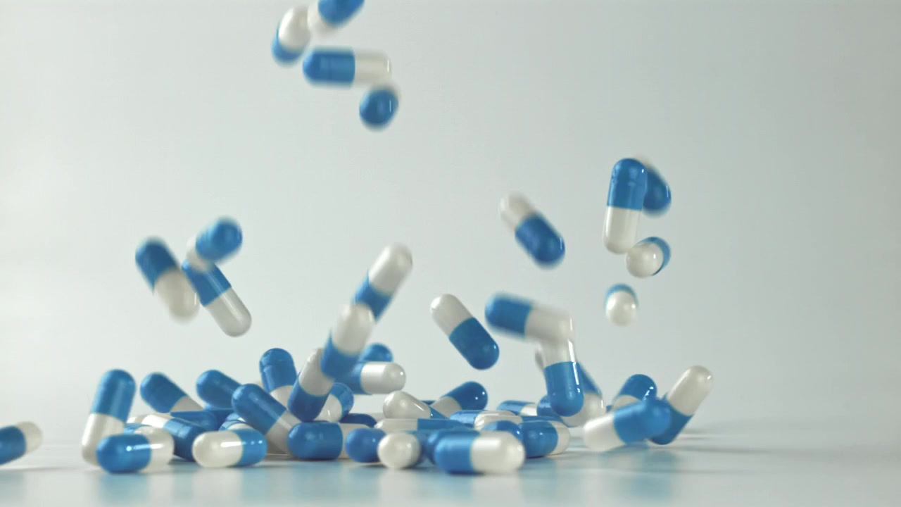 Capsule blu e bianche che cadono e si disperdono su una superficie bianca