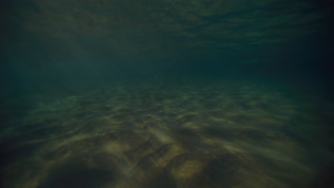 Underwater-ocean-background-with-sandy-bottom-and-dancing-light-rays-under-breaking-wave