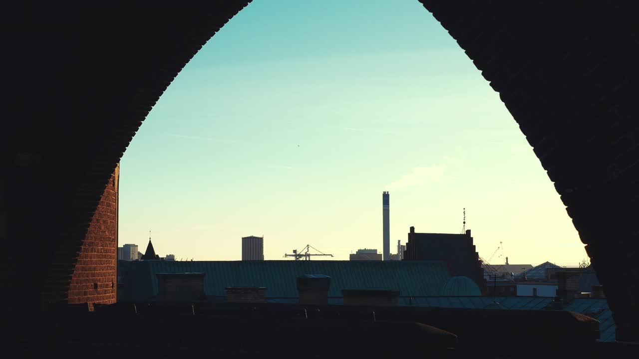 City view from brick wall window at dusk. Smokestack and silo, Helsingborg, Sweden