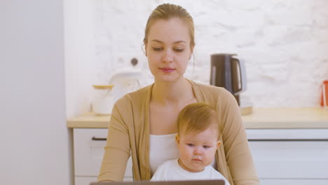 Porträt-Einer-Jungen-Frau,-Die-An-Einem-Laptop-Arbeitet,-Während-Sie-Zu-Hause-Mit-Einem-Kleinen-Jungen-Sitzt