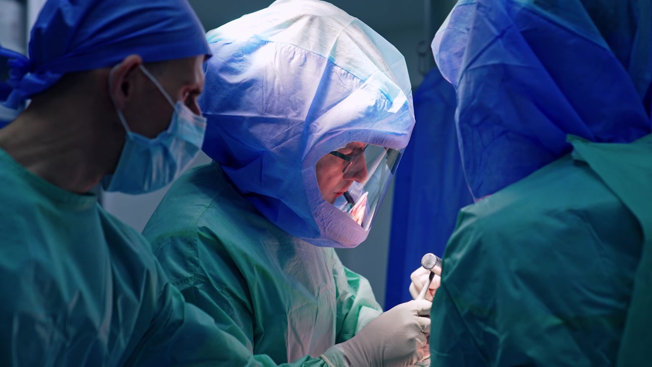 Il chirurgo capo usa un martello metallico in chirurgia artroscopica. Medici con caschi protettivi eseguono un'operazione ortopedica.