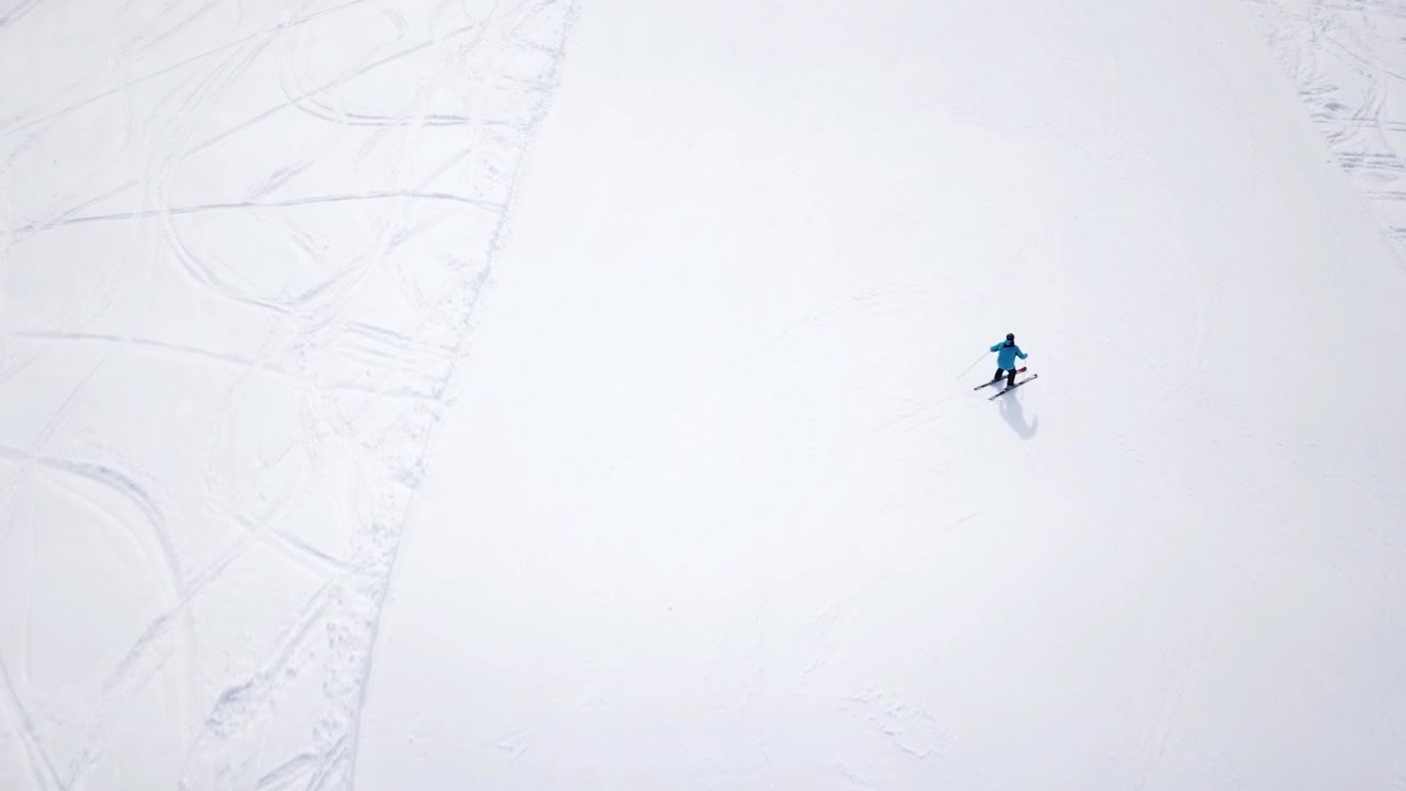 Aerial - Top view tracking shot of good alpine skier skiing down the wide ski slope alone
