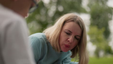 a woman wearing a light blue dress appears to be blowing air at something intently, a partial blurred view of someone near her is also visible in the foreground