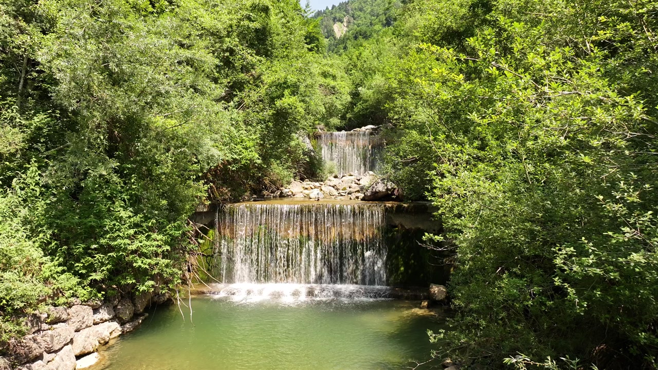 Peaceful waterfall in lush green forest near Walensee, Switzerland, fresh water flowing into pond, drone pushes back.