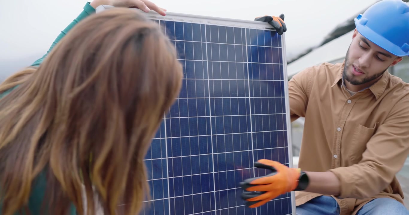 Installatore che usa una pinza e guanti per posizionare un pannello solare sul tetto, con il proprietario di casa che ispeziona il posizionamento.