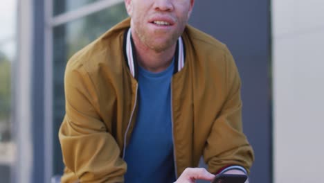 Thoughtful-albino-african-american-man-with-dreadlocks-on-bike-using-smartphone