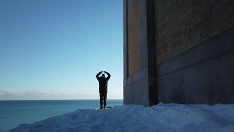 Wide-shot-of-parka-clad-man-doing-jumping-jacks-on-a-sunny-hilltop-overlooking-Lake-Ontario