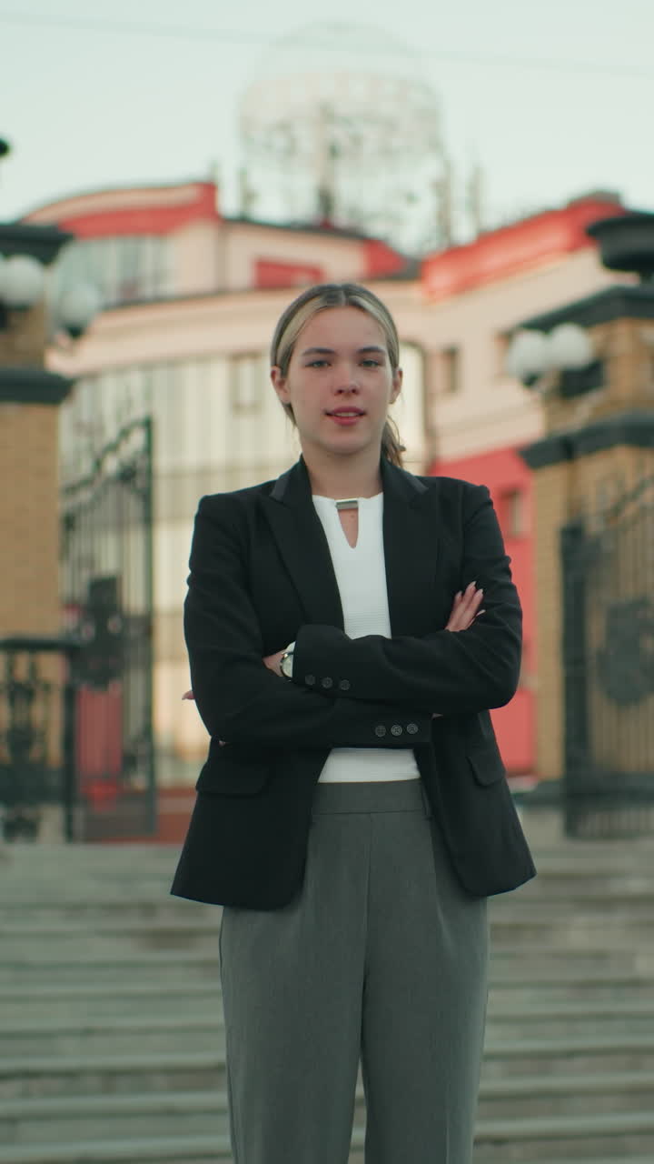 Confident white lady standing with arms crossed in urban setting, dressed professionally, exuding boldness and composure, with architectural elements and stairs in background