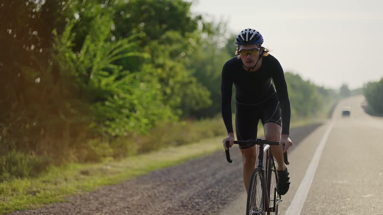 Ciclista uomo con casco che pedala lungo la pista, supera la salita