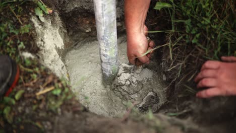 worker uses concrete trowel to spread mixture around steel pipe dug into ground