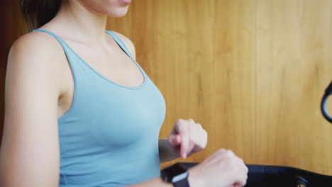 mujer haciendo ejercicio en la cinta de correr en casa usando auriculares inalámbricos comprobando reloj inteligente