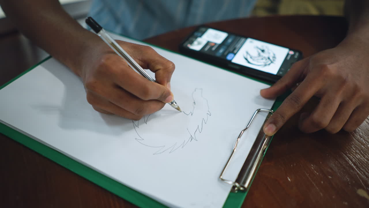 Closer view of hand sketching detailed drawing on white paper with smartphone image reference positioned nearby for inspiration while pencil glides across page capturing creative process in focused