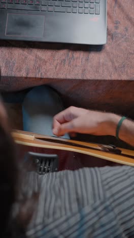 close-up of a person playing an acoustic guitar with a laptop nearby