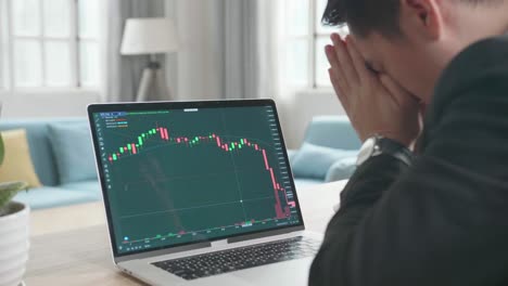 un hombre de negocios asiático con traje de negocios está molesto después de ver caer los precios de las acciones en la negociación en la pantalla de la computadora mientras trabaja en casa.