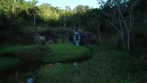 Drone-footage-of-lake-with-vegetation-in-the-water-and-beautiful-waterfall-in-the-background,-water-reflection,-peace,-serenity,-in-4k-resolution