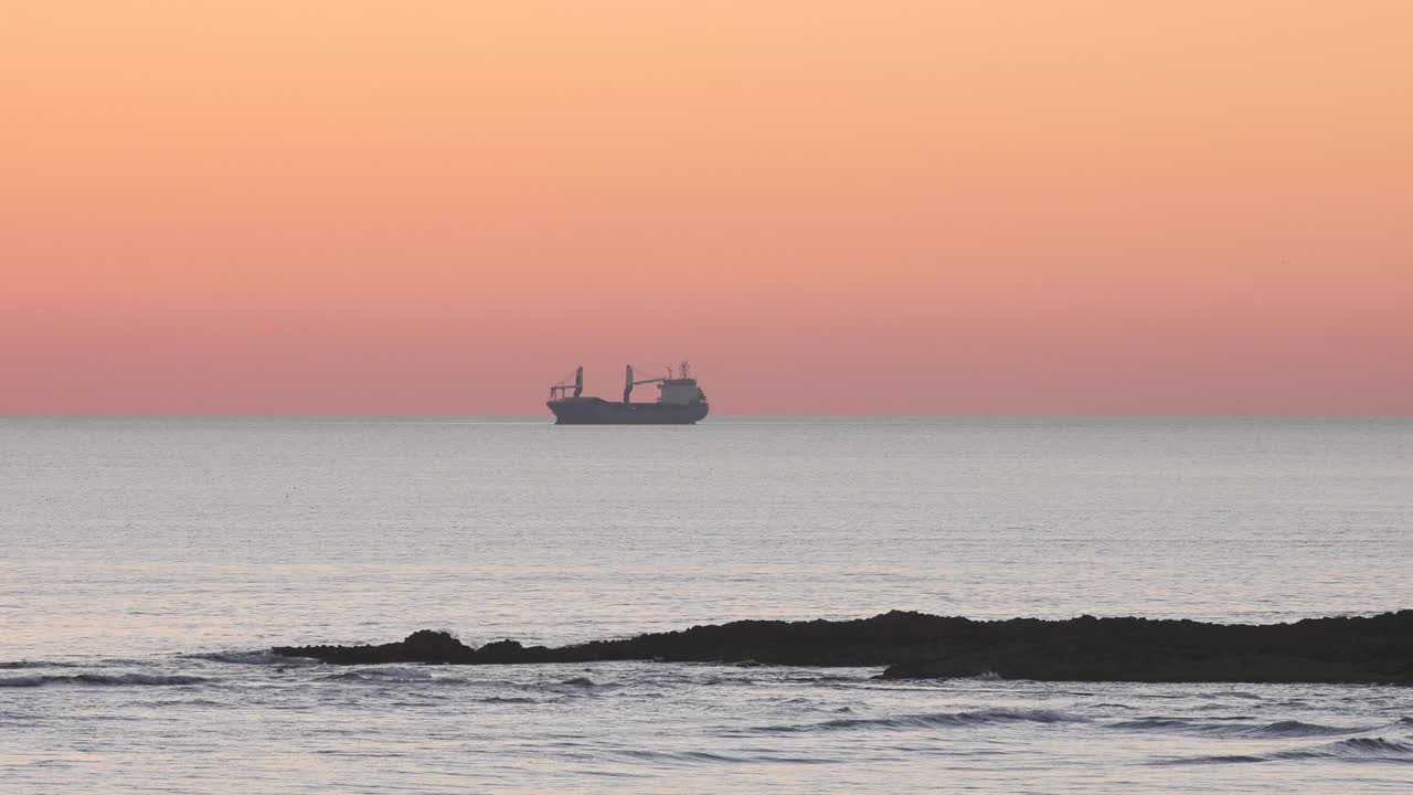 작은 파도가 있는 일출 또는 일몰의 고요한 해변, 수평선 위의 보트, 멋진 주황색 하늘, 카르카벨로스, 카스카이스에서 목가적이고 평화로운 분위기를 조성합니다.