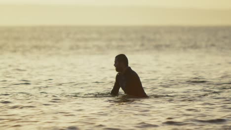 side view of mid-adult caucasian male surfer sitting over surfboard in sea during sunset 4k