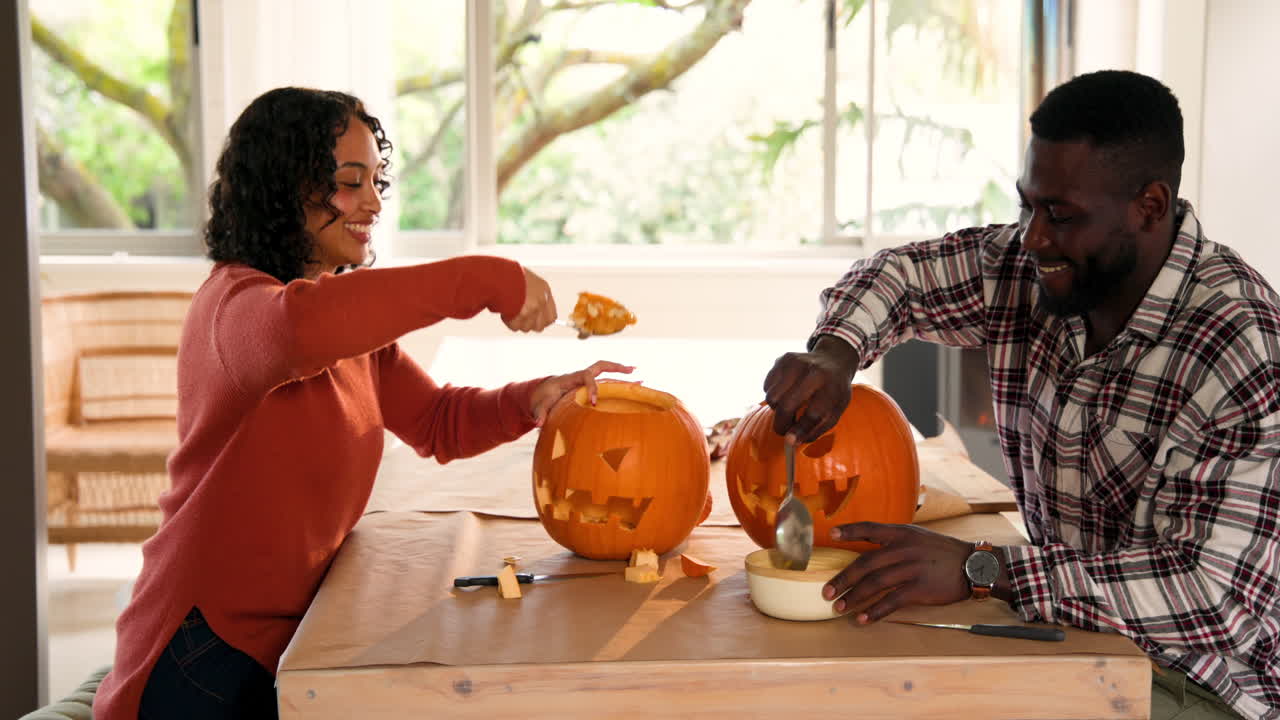 Halloween time, smiling multiracial couple carving pumpkins together at home