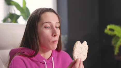 happy young woman sitting at desk and eating rice crackers