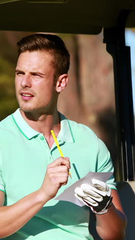 golfista sentado en un buggy de golf escribiendo en papel