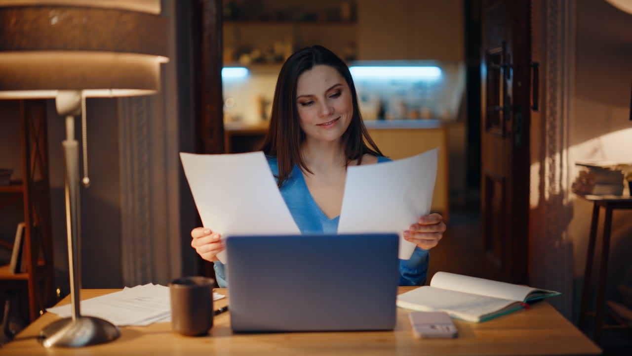 Smiling entrepreneur examining documents sitting laptop at dark room closeup