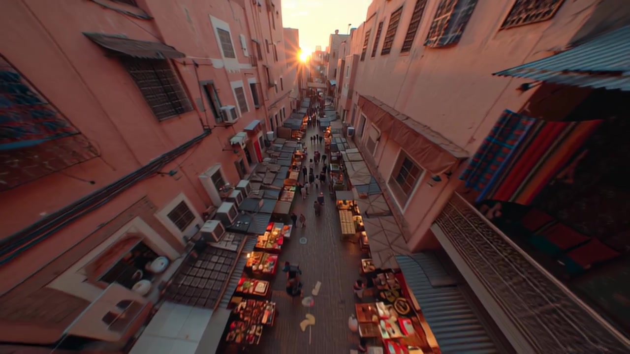 High-angle aerial footage of a narrow market street with stalls and crowds between traditional buildings at golden hour, ideal for travel, culture, and tourism themes