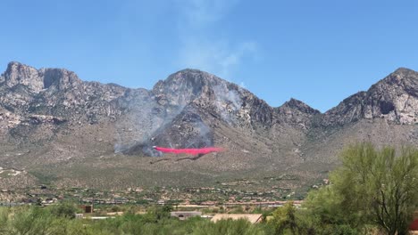 firefighters airplane flying under wildfire dropping retardant preventing spread in valley under mountain hills