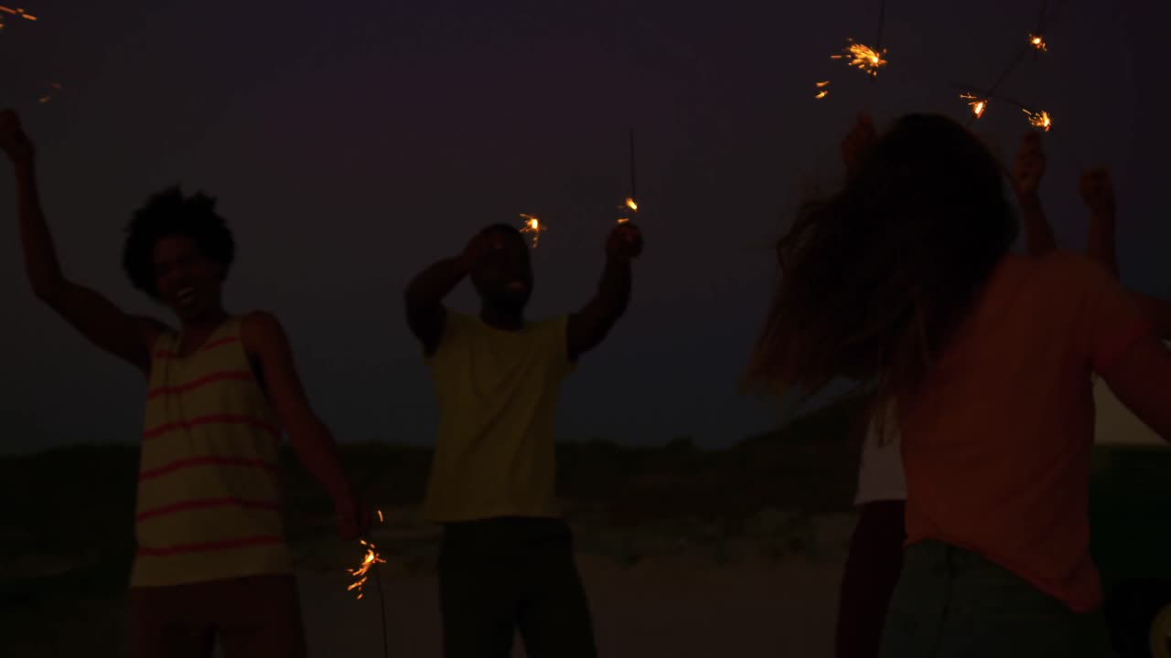 jóvenes amigos adultos divirtiéndose en la playa por la noche con chispas 4k