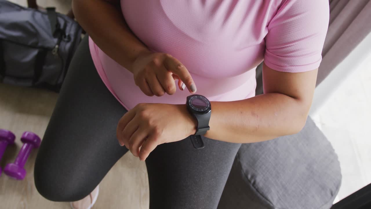 Video of midsection of plus size african american woman in sport clothes checking smartwatch