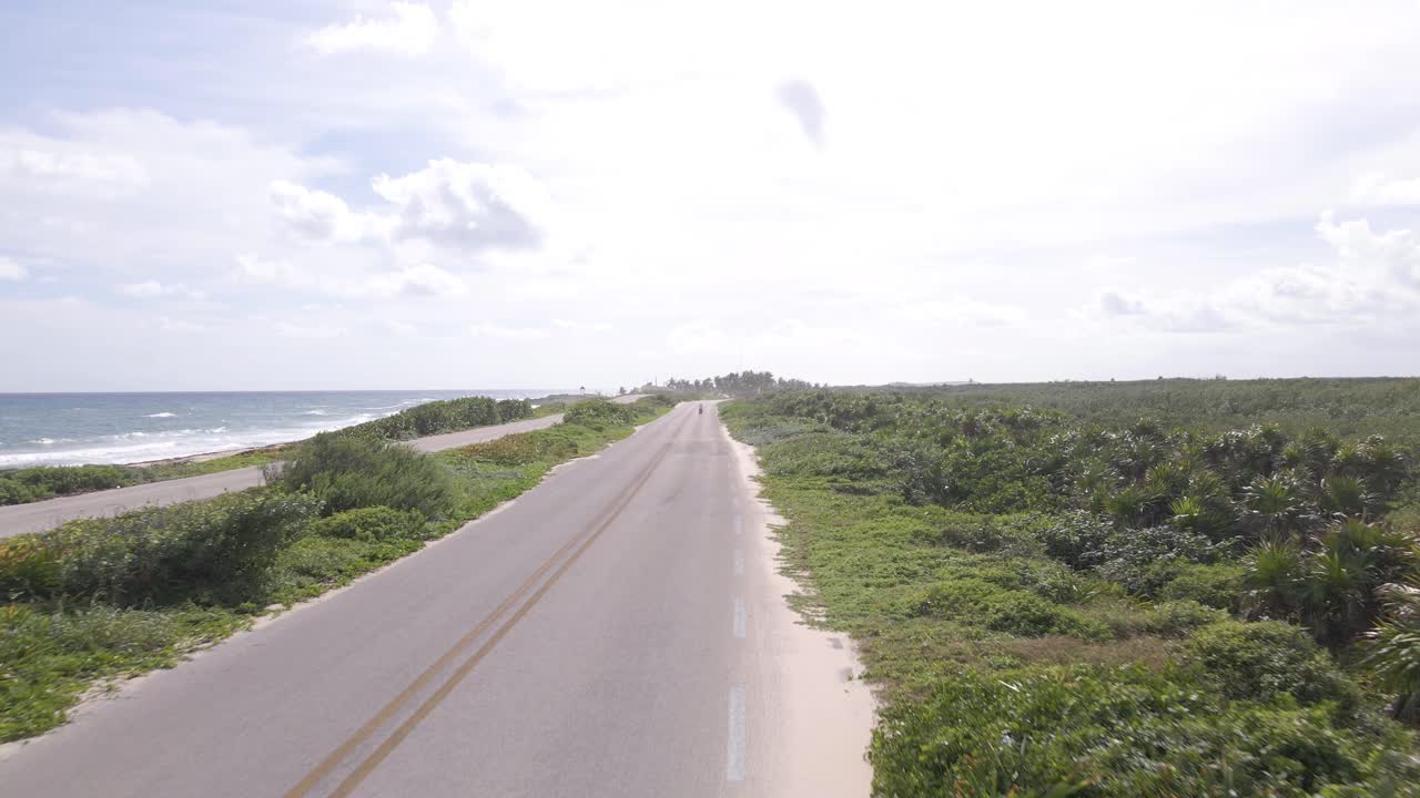 Low drone shot revealing a young women driving a red scooter down the highway off the coast of the beautiful tropical Island of Cozumel, Mexico shot in 4k