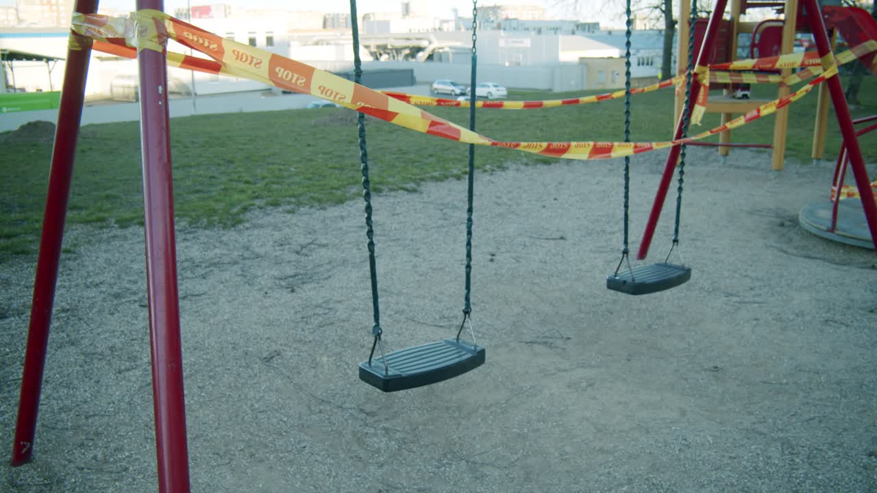 A Closed Down Swing Seat in an Empty Kids' Playground Wrapped in Yellow and Red "STOP" Caution Tape due to Quarantine