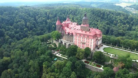 wide aerial pullback of ksiaz castle in poland, red-roofed structure among dense forest landscape
