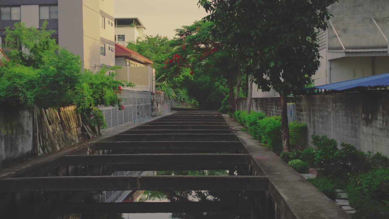 A tranquil scene of a canal extending through an urban area, framed by greenery and adjacent buildings, captured during golden hour with warm light and serene atmosphere.