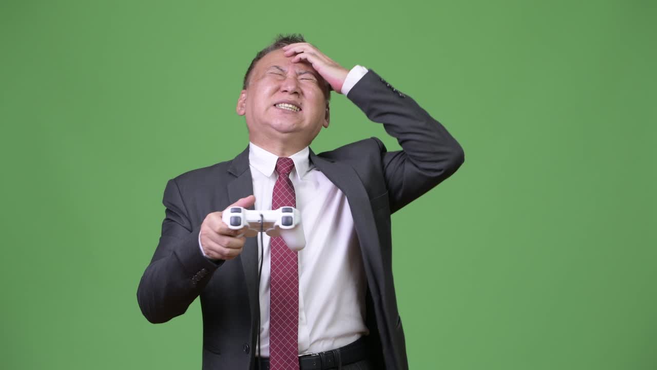 성숙 한 일본인 사업가 가 초록색 배경 에 게임 을 하고 있다