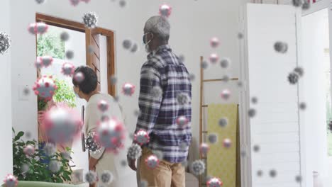 Multiple-covid-19-cells-floating-against-african-american-couple-welcoming-caucasian-couple-at-home