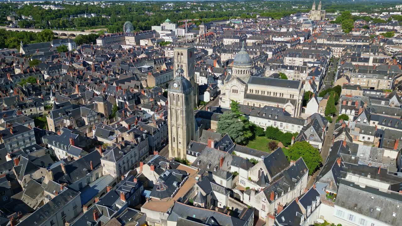 Cityscape aerial featuring the Basilica of Saint Martin in Tours, France, rising above colorful residential rooftops under a sunny sky, blending historic architecture and modern urban life