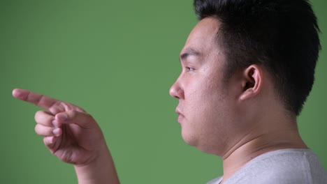 young handsome overweight asian man against green background