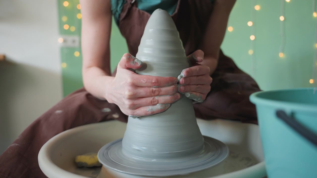 Vasaio che crea un vaso. Una donna modella un recipiente ceramico rotondo. Un'artista modella ceramiche a forma di cono sul tornio. Un'artista modella con cura un recipiente di argilla conico con luci di sfondo brillanti