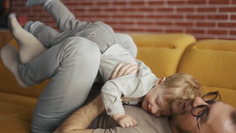 hombre alegre sosteniendo saltar niño pequeño divirtiéndose juntos en el sofá en la sala de estar