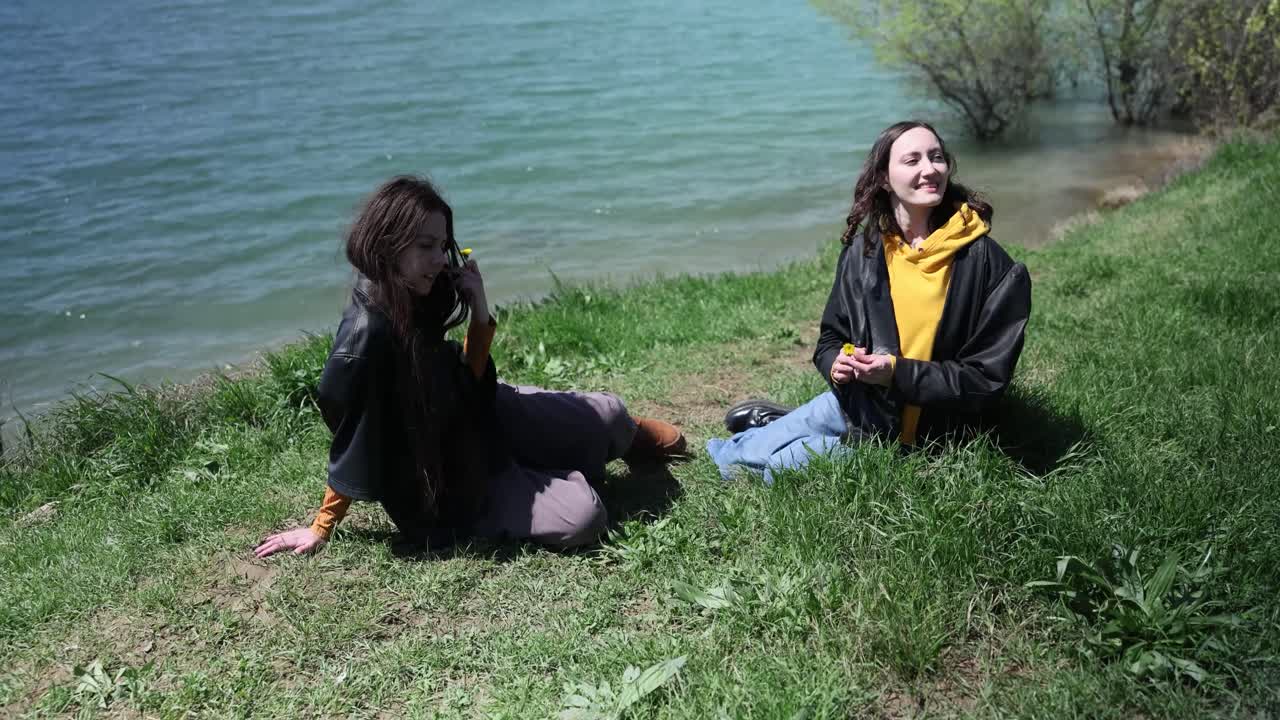 To unge kvinder slapper af og taler ved en sø på en solrig dag